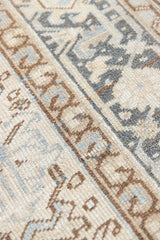 A close up of the arabesque boarder. The Portia rug features an intricate all over Heriz design comprised of floral and palmette motifs set against a taupe ground and muted blue toned boarder. A beautiful antique carpet.