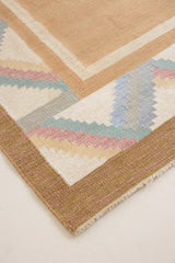 A Swedish geometric-patterned rug with multicolor border on a beige background. This röllakan rug was handwoven by the mid-century textile designer Anna Johanna Angström.