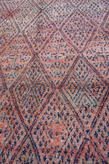 Beni M’guild thick piled carpet. Rug features a dark blue geometric pattern on a peachy pink background.