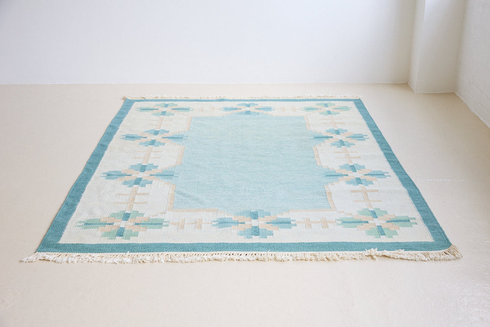 Elio is a pretty blue Swedish flatweave, featuring a bold geometric floral design with hints of beige and pink within the motifs.