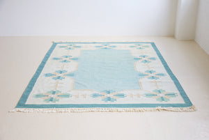 Elio is a pretty blue Swedish flatweave, featuring a bold geometric floral design with hints of beige and pink within the motifs.