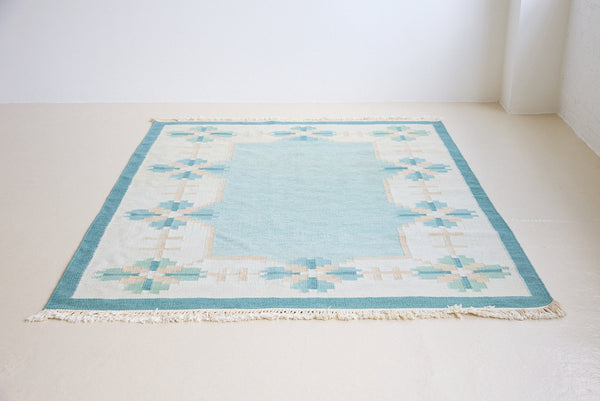 Elio is a pretty blue Swedish flatweave, featuring a bold geometric floral design with hints of beige and pink within the motifs.