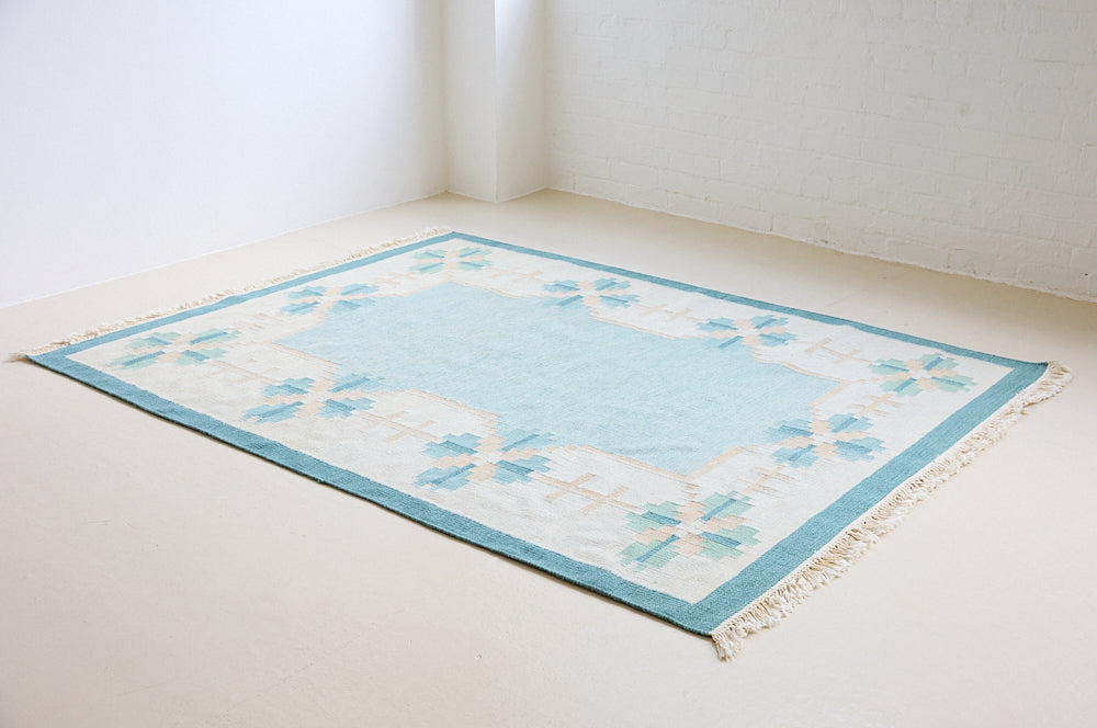 Elio is a pretty blue Swedish flatweave, featuring a bold geometric floral design with hints of beige and pink within the motifs.