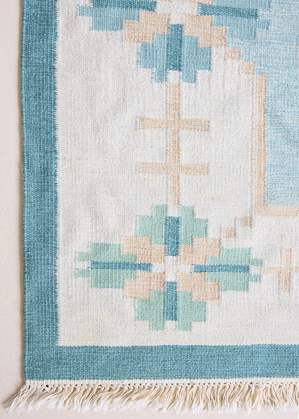 Elio is a pretty blue Swedish flatweave, featuring a bold geometric floral design with hints of beige and pink within the motifs.
