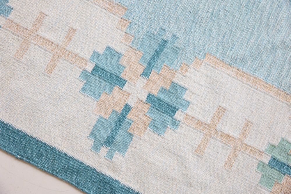 Elio is a pretty blue Swedish flatweave, featuring a bold geometric floral design with hints of beige and pink within the motifs.