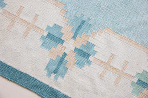 Elio is a pretty blue Swedish flatweave, featuring a bold geometric floral design with hints of beige and pink within the motifs.