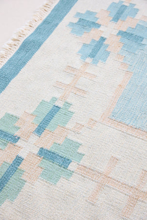 Elio is a pretty blue Swedish flatweave, featuring a bold geometric floral design with hints of beige and pink within the motifs.