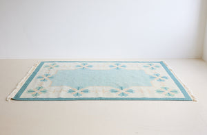 Elio is a pretty blue Swedish flatweave, featuring a bold geometric floral design with hints of beige and pink within the motifs.