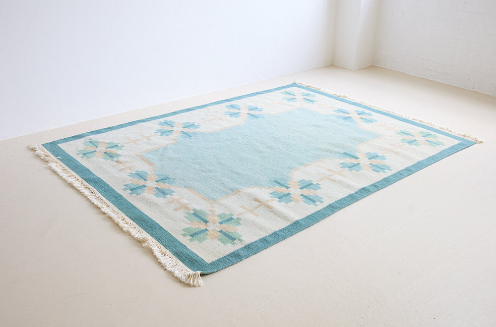 Elio is a pretty blue Swedish flatweave, featuring a bold geometric floral design with hints of beige and pink within the motifs.