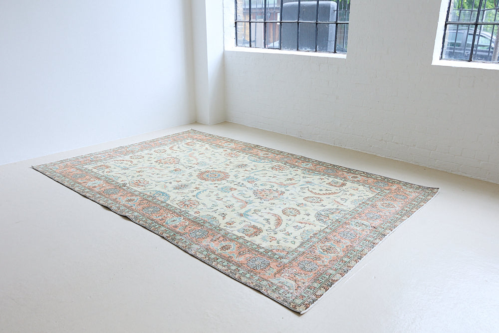Genevieve is a vintage Turkish Oushak rug. Oushaks are defined by their softness in palette and large-scale, open compositions.The muted beige field is decorated with pretty floral scrolls, framed by a soft pinky red border.