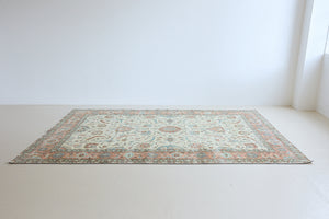 Genevieve is a vintage Turkish Oushak rug. Oushaks are defined by their softness in palette and large-scale, open compositions.The muted beige field is decorated with pretty floral scrolls, framed by a soft pinky red border.