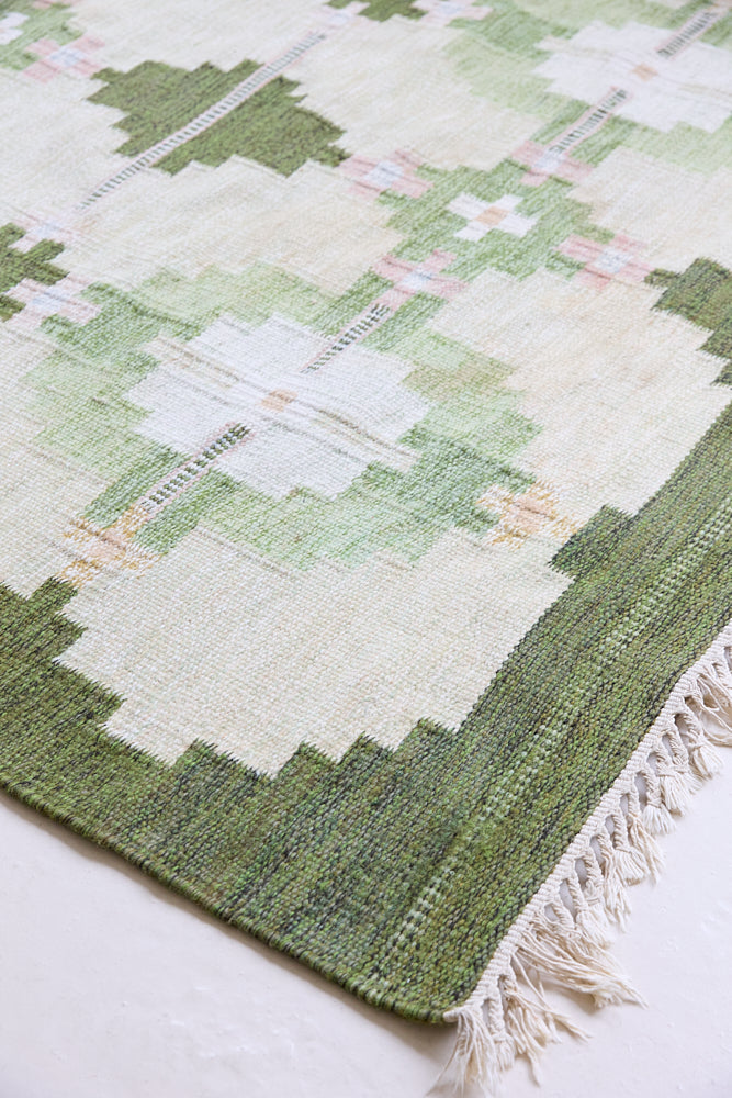 Jensen is a vintage rug handwoven in Sweden featuring a bold geometric pattern on a green field. The kilim is signed HLO.