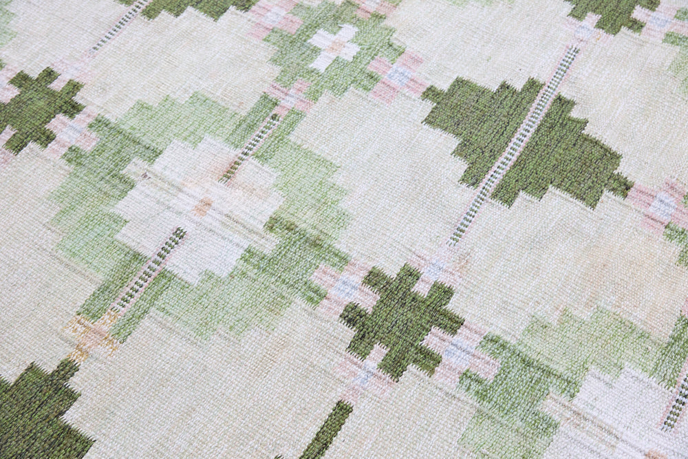 Jensen is a vintage rug handwoven in Sweden featuring a bold geometric pattern on a green field. The kilim is signed HLO.