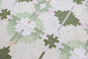 Jensen is a vintage rug handwoven in Sweden featuring a bold geometric pattern on a green field. The kilim is signed HLO.