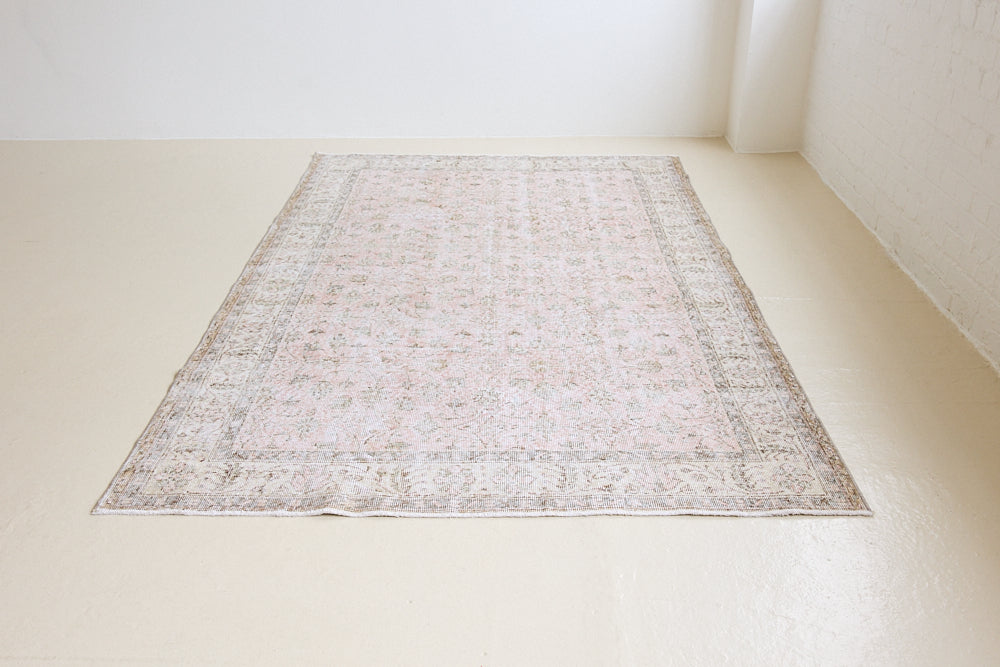 Lizzie is a vintage wool rug handwoven in Turkey approximately 70 years ago. The soft pink field and is decorated with an all floral scrolls pattern framed by a subtle contrasting taupe boarder.