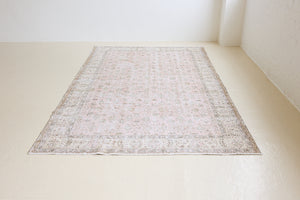 Lizzie is a vintage wool rug handwoven in Turkey approximately 70 years ago. The soft pink field and is decorated with an all floral scrolls pattern framed by a subtle contrasting taupe boarder.