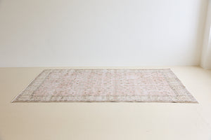 Lizzie is a vintage wool rug handwoven in Turkey approximately 70 years ago. The soft pink field and is decorated with an all floral scrolls pattern framed by a subtle contrasting taupe boarder.