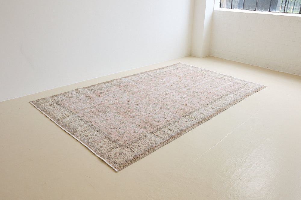 Lizzie is a vintage wool rug handwoven in Turkey approximately 70 years ago. The soft pink field and is decorated with an all floral scrolls pattern framed by a subtle contrasting taupe boarder.