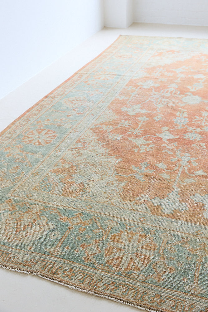 An antique Turkish Oushak rug. Perdita features a large-scale, open medallion pattern, flowing botanical motifs and a generous field space set against a blue and terracotta ground.