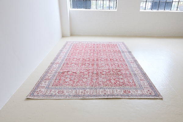 Teresa is a vintage rug handwoven in Turkey approximately 80 years ago. The warm red field and soft blue and beige border are intertwined with an all over flowering vine pattern.