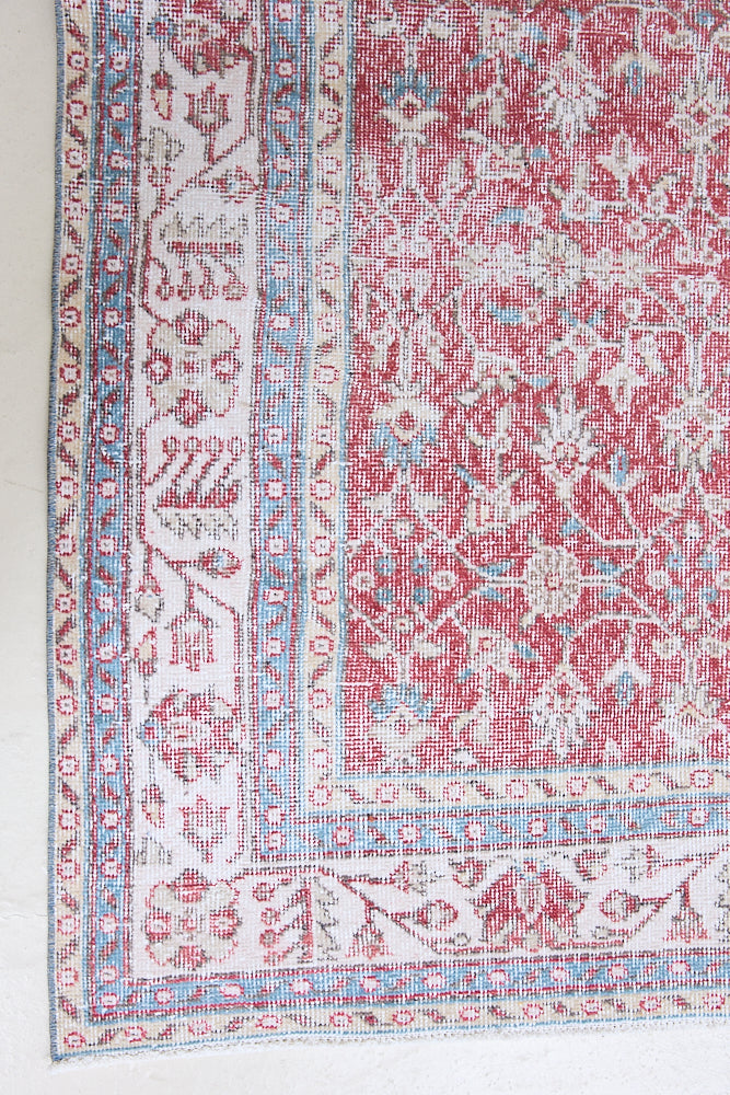 Teresa is a vintage rug handwoven in Turkey approximately 80 years ago. The warm red field and soft blue and beige border are intertwined with an all over flowering vine pattern.