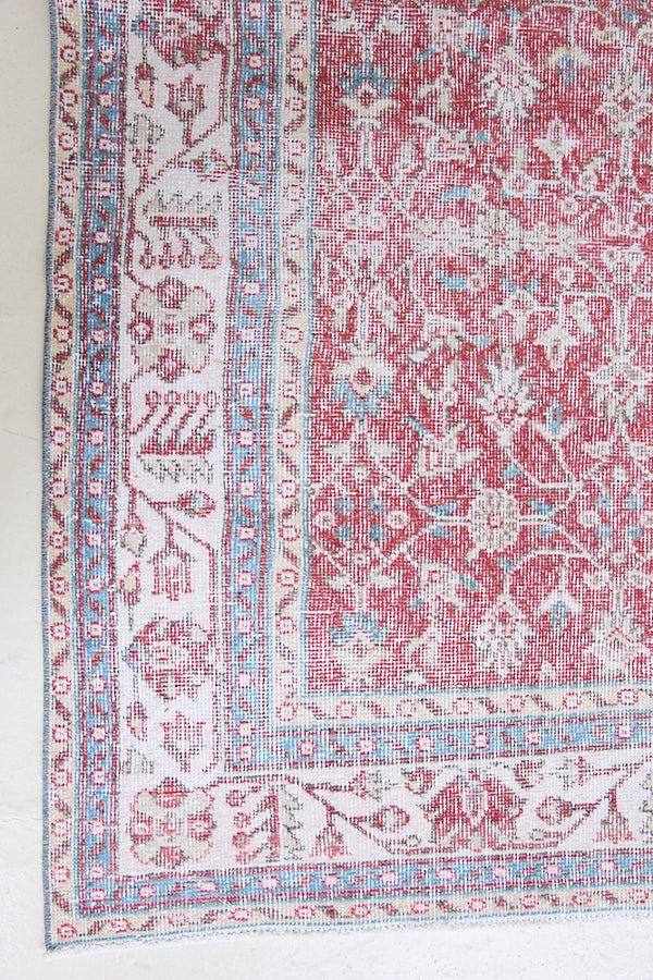 Teresa is a vintage rug handwoven in Turkey approximately 80 years ago. The warm red field and soft blue and beige border are intertwined with an all over flowering vine pattern.