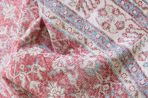 Teresa is a vintage rug handwoven in Turkey approximately 80 years ago. The warm red field and soft blue and beige border are intertwined with an all over flowering vine pattern.