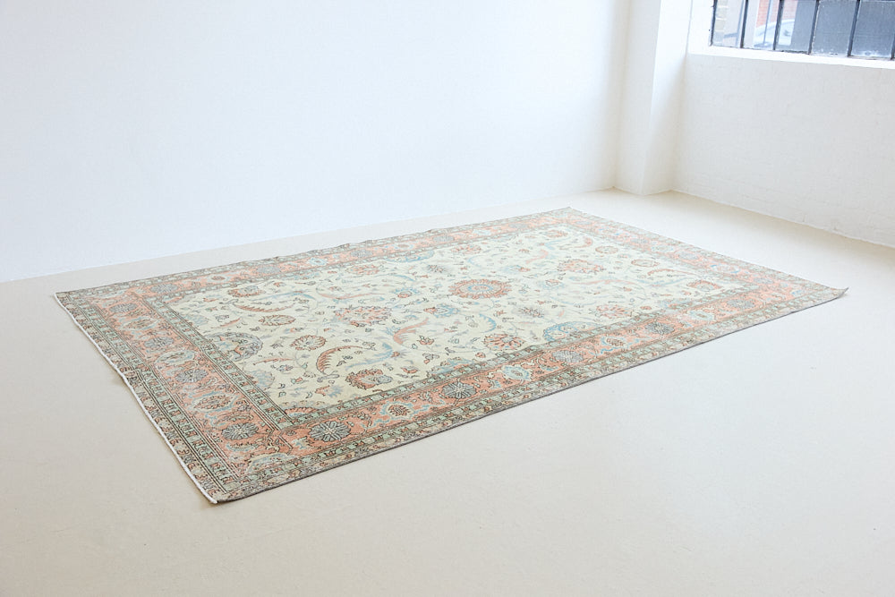 Genevieve is a vintage Turkish Oushak rug. Oushaks are defined by their softness in palette and large-scale, open compositions.The muted beige field is decorated with pretty floral scrolls, framed by a soft pinky red border.