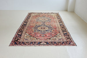 Camille is an antique hand-woven Ushak rug with two central medallions floating on a muted field of rust and taupe, anchored by a striking black floral border.