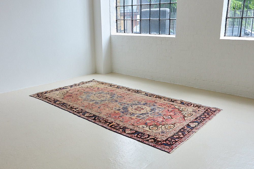 Camille is an antique hand-woven Ushak rug with two central medallions floating on a muted field of rust and taupe, anchored by a striking black floral border.
