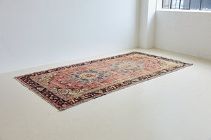 Camille is an antique hand-woven Ushak rug with two central medallions floating on a muted field of rust and taupe, anchored by a striking black floral border.