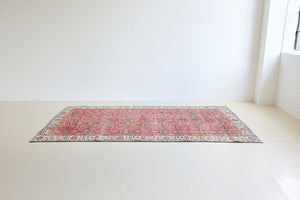 Glenda is a vintage wool rug handwoven in Turkey approximately 80 years ago. The warm terracotta field and is decorated with an all floral scrolls pattern framed by a contrasting taupe boarder.