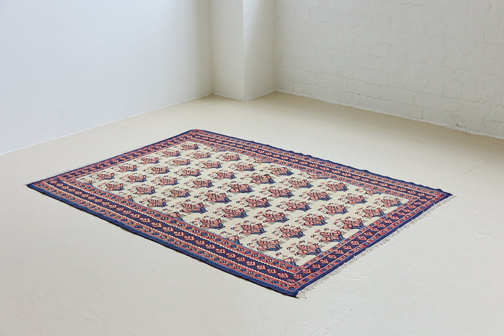 Isolde is a vintage geometric Anatolian kilim rug. Hand-woven on village and nomadic looms in vivid, naturally dyed colours, a tradition stretching back thousands of years. Kilims were woven for the practicalities of daily life and used as floor and wall coverings, storage bags, and prayer mats. Isolde features a pretty pink floral motif across a taupe field with a contrasting dark blue boarder.