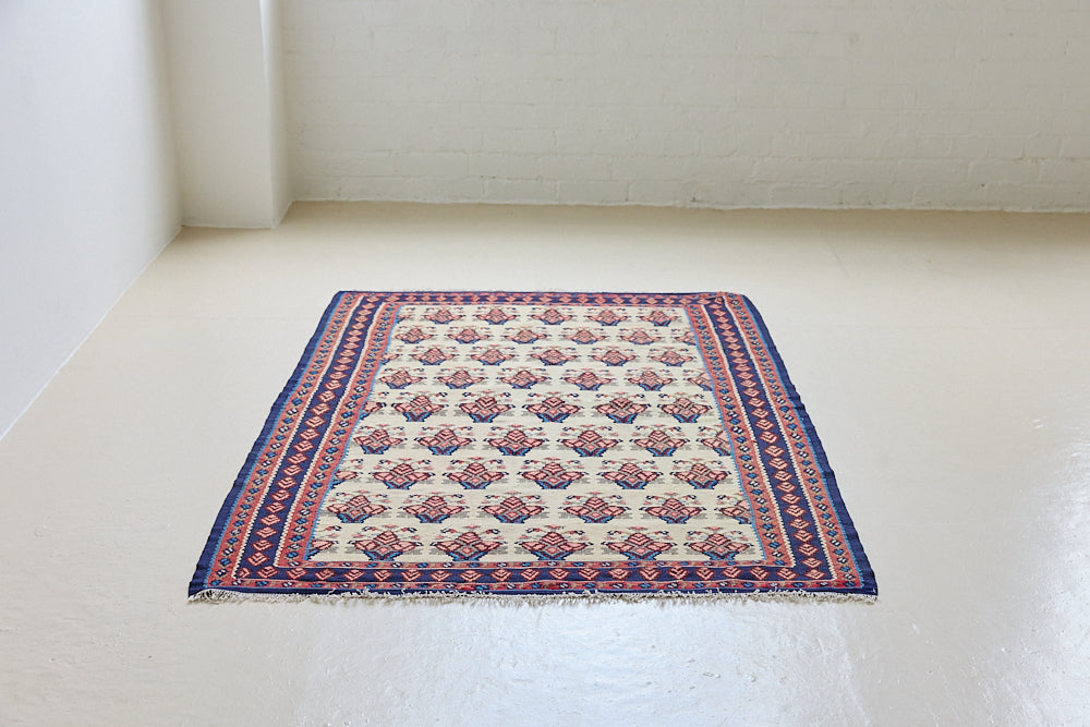 Isolde is a vintage geometric Anatolian kilim rug. Hand-woven on village and nomadic looms in vivid, naturally dyed colours, a tradition stretching back thousands of years. Kilims were woven for the practicalities of daily life and used as floor and wall coverings, storage bags, and prayer mats. Isolde features a pretty pink floral motif across a taupe field with a contrasting dark blue boarder.