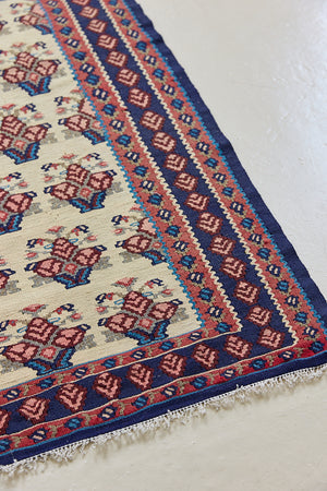 Isolde is a vintage geometric Anatolian kilim rug. Hand-woven on village and nomadic looms in vivid, naturally dyed colours, a tradition stretching back thousands of years. Kilims were woven for the practicalities of daily life and used as floor and wall coverings, storage bags, and prayer mats. Isolde features a pretty pink floral motif across a taupe field with a contrasting dark blue boarder.