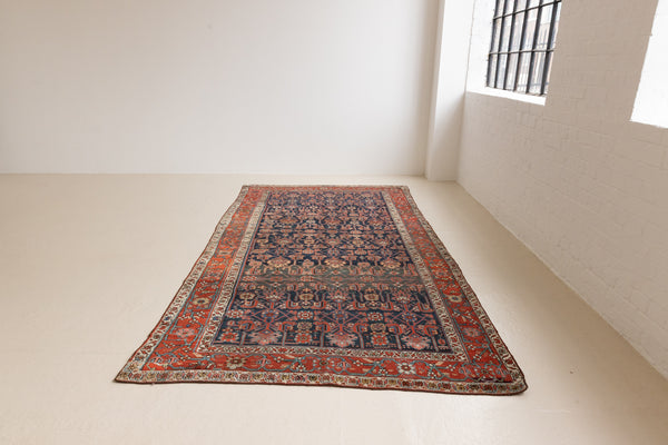 This is a Persian Mahal carpet which are known for decorative designs and repeating floral patterns. This Vintage hand woven rug features a midnight navy ground complimented by a rich red border.