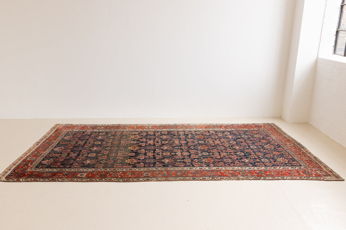 This is a Persian Mahal carpet which are known for decorative designs and repeating floral patterns. This Vintage hand woven rug features a midnight navy ground complimented by a rich red border.