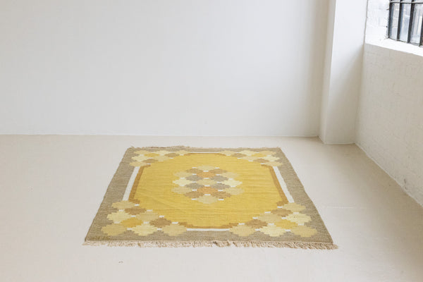 This is an original vintage Swedish flat weave carpet signed by the renowned textile designer Karin Jonsson. This rug features a palette of rich ochre yellow and a beautiful geometric design. 
