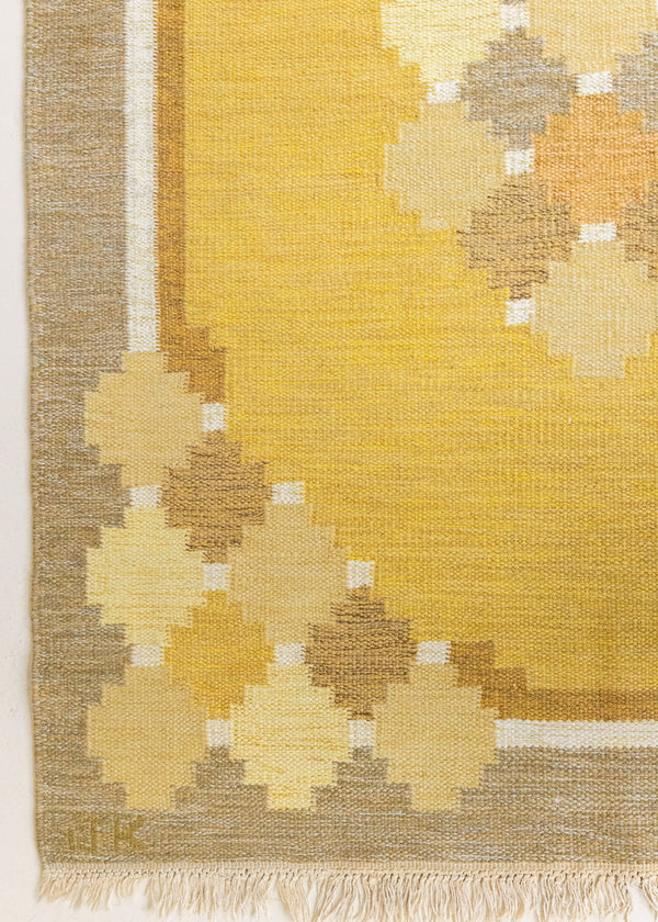 This is an original vintage Swedish flat weave carpet signed by the renowned textile designer Karin Jonsson. This rug features a palette of rich ochre yellow and a beautiful geometric design. 