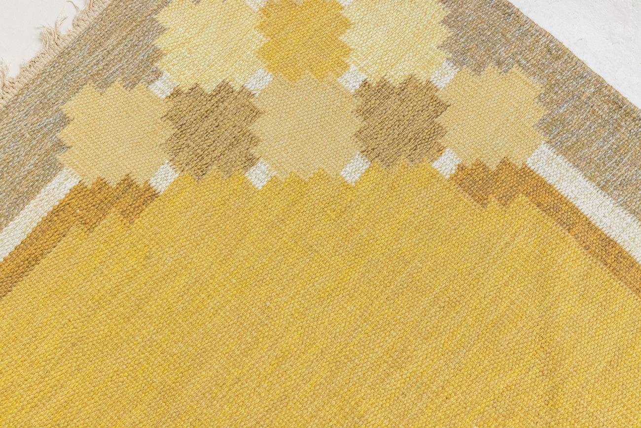 This is an original vintage Swedish flat weave carpet signed by the renowned textile designer Karin Jonsson. This rug features a palette of rich ochre yellow and a beautiful geometric design. 