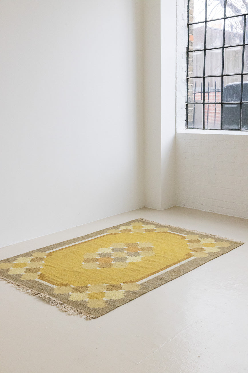 This is an original vintage Swedish flat weave carpet signed by the renowned textile designer Karin Jonsson. This rug features a palette of rich ochre yellow and a beautiful geometric design. 
