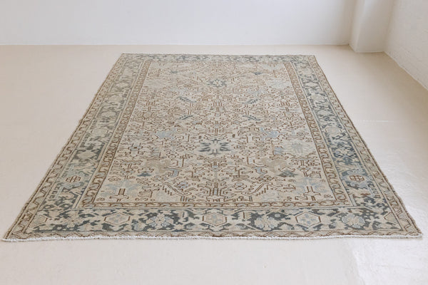 The Portia rug features an intricate all over Heriz design comprised of floral and palmette motifs set against a taupe ground and muted blue toned boarder. A beautiful antique carpet.