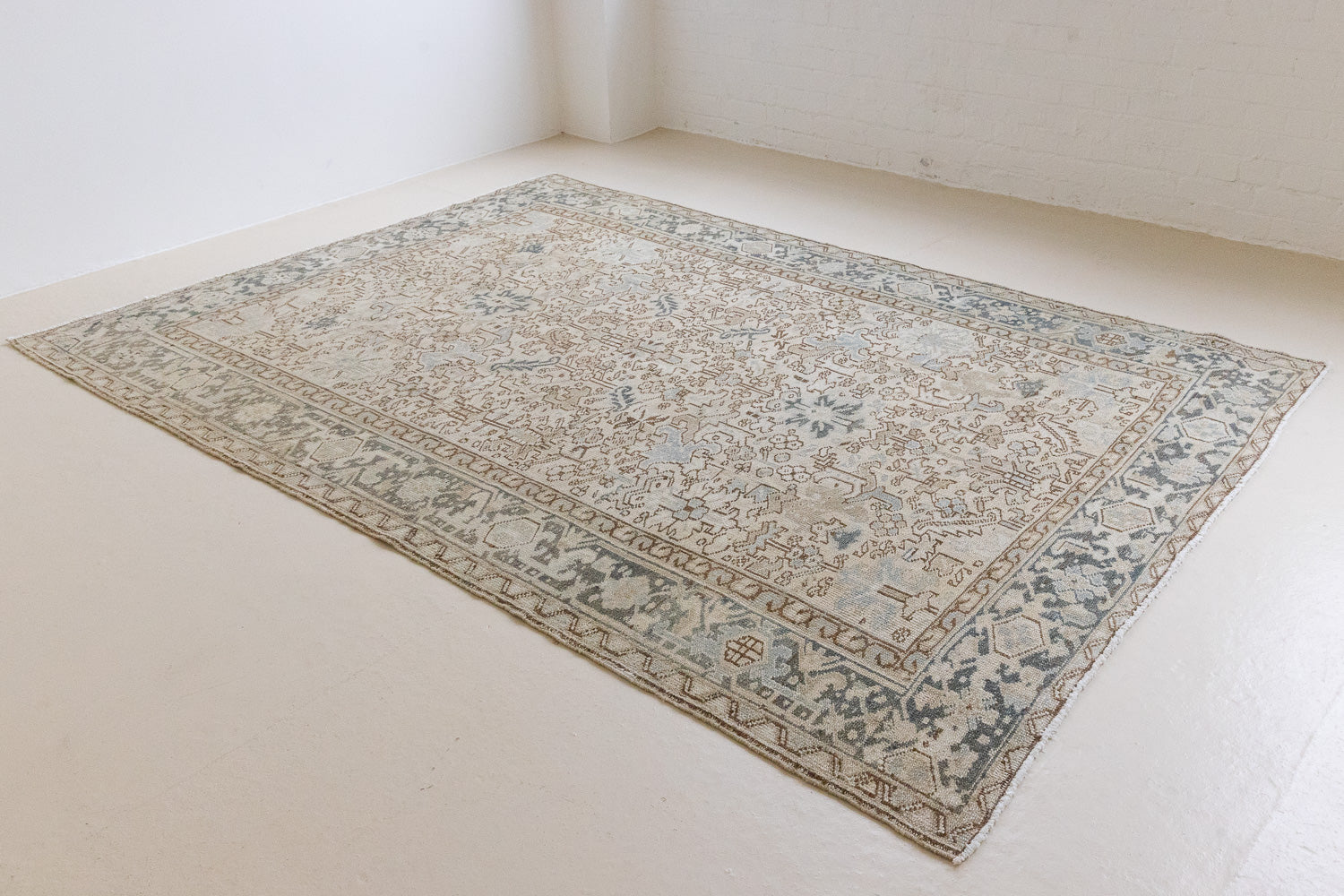 The Portia rug features an intricate all over Heriz design comprised of floral and palmette motifs set against a taupe ground and muted blue toned boarder. A beautiful antique carpet.