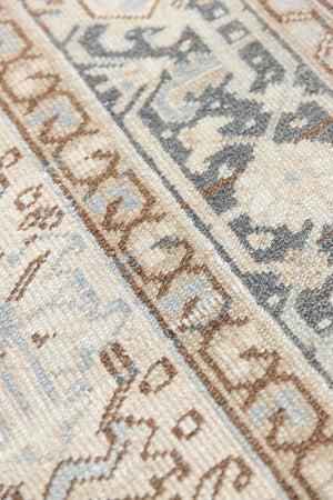 A close up of the arabesque boarder. The Portia rug features an intricate all over Heriz design comprised of floral and palmette motifs set against a taupe ground and muted blue toned boarder. A beautiful antique carpet. 