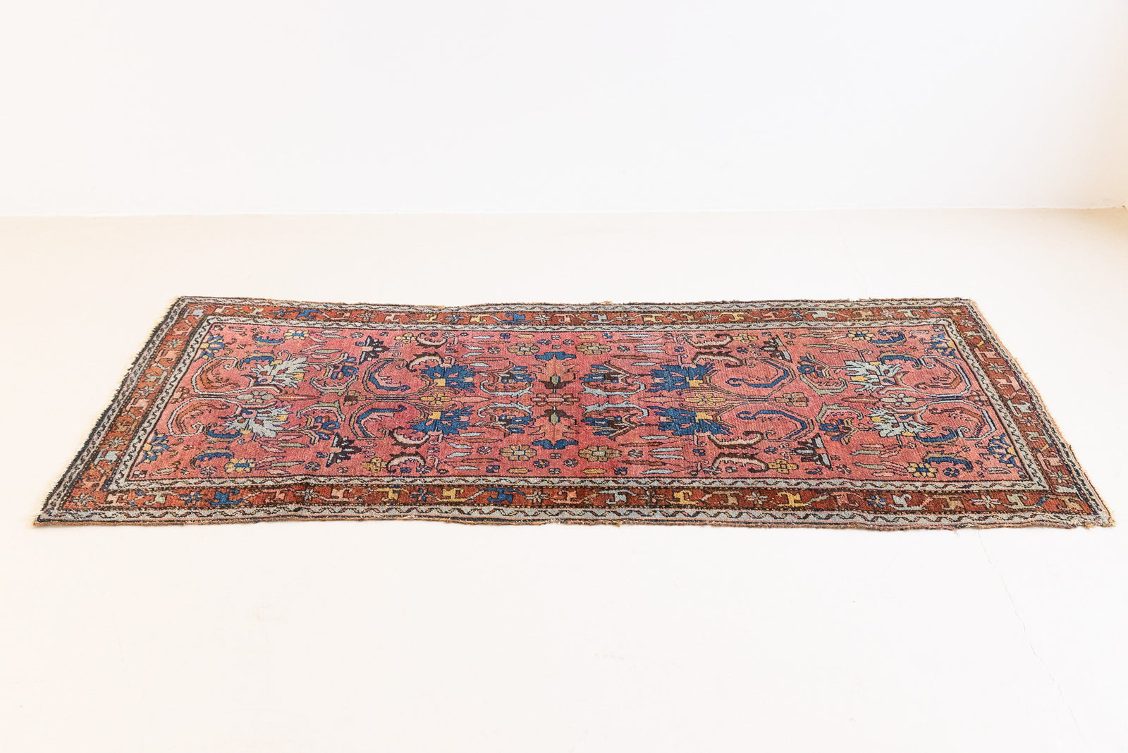 This Vintage rug was handwoven in a small village in Western Persia and features floral and geometric patterns and hints of pink and blue.