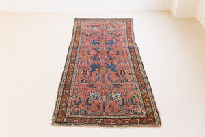 This Vintage rug was handwoven in a small village in Western Persia and features floral and geometric patterns and hints of pink and blue.