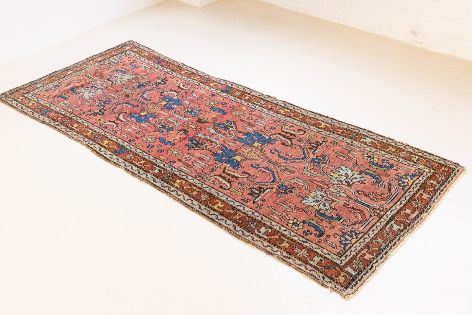 This Vintage rug was handwoven in a small village in Western Persia and features floral and geometric patterns and hints of pink and blue.