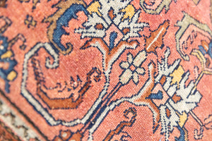 This Vintage rug was handwoven in a small village in Western Persia and features floral and geometric patterns and hints of pink and blue.