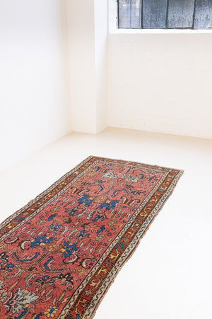 This Vintage rug was handwoven in a small village in Western Persia and features floral and geometric patterns and hints of pink and blue.