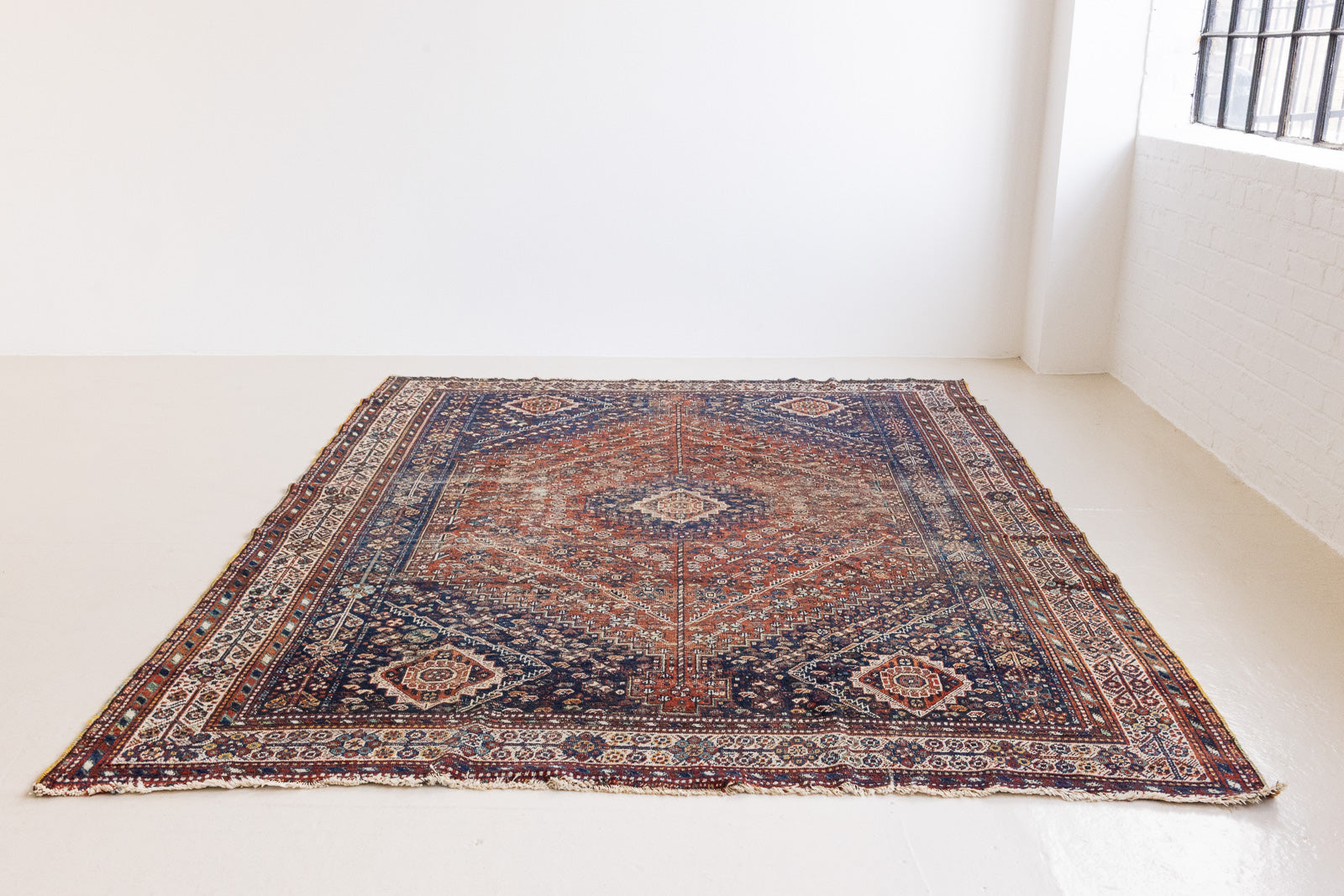 A Qashqai carpet. Sydney features a striking central diamond medallion, a classic motif in Qashqai weaving, framed by a repeating floral, boteh and gul pattern.